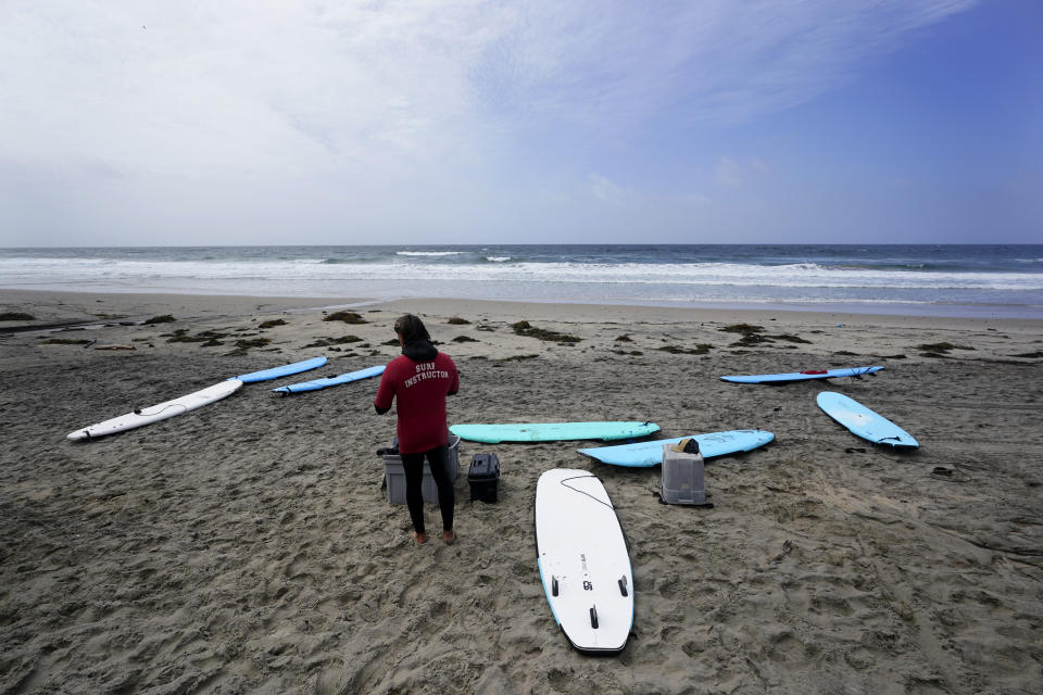 Surf instructor Ken Gettenio awaits students on an empty Pacific Beach in between rain storms, Tuesday, March 21, 2023, in San Diego. Californians are tired. Tired of the rain, tired of the snow, tired of stormy weather and the cold, relentlessly gray skies that have clouded the Golden State nearly nonstop since late December. (AP Photo/Gregory Bull)