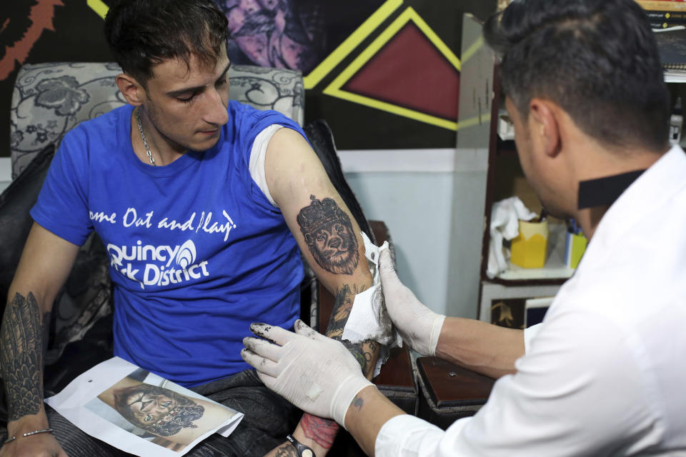 In this Wednesday, Nov. 20, 2019, photo, Omid Noori, 23, left, gets a lion tattoo on his left arm by Nazeer Mosawi, a tattoo artist in Kabul, Afghanistan. Mosawi, 42, fought for seven years in Afghanistan’s civil war with the Islamic insurgents. He says he is still fighting the war, but this time his battle is against society’s conservatism, with his tattoo machine as his weapon. (AP Photo/Rahmat Gul)