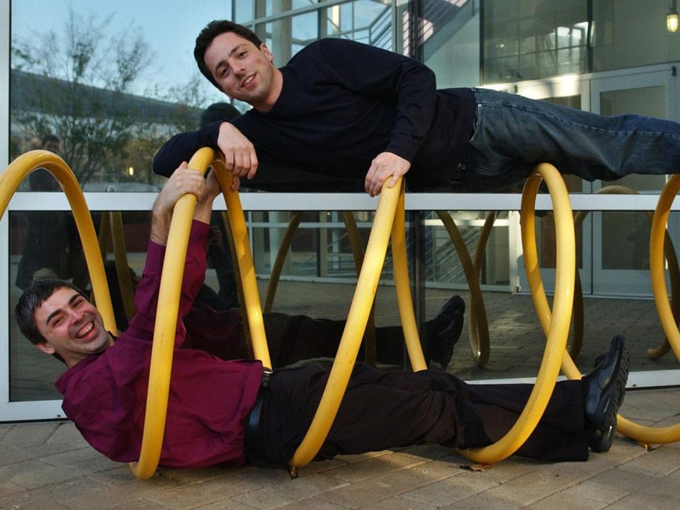 Larry Page and Sergey Brin laying inside and on top of a yellow spiral tube