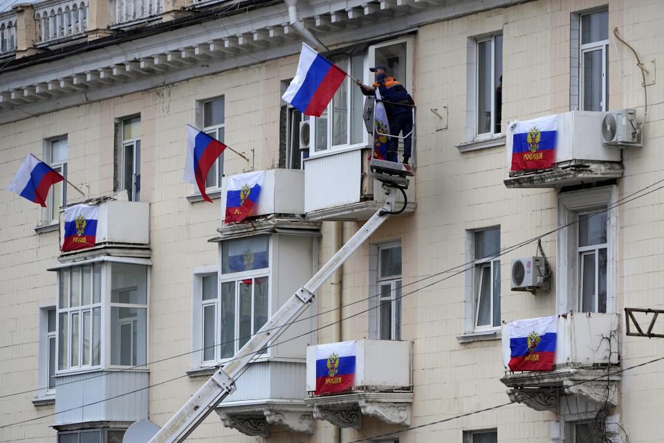 Workers hang Russian flags at an apartment building in Luhansk, Luhansk People's Republic controlled by Russia-backed separatists, eastern Ukraine, Tuesday, Sept. 27, 2022. Voting began Friday in four Moscow-held regions of Ukraine on referendums to become part of Russia. (AP Photo)