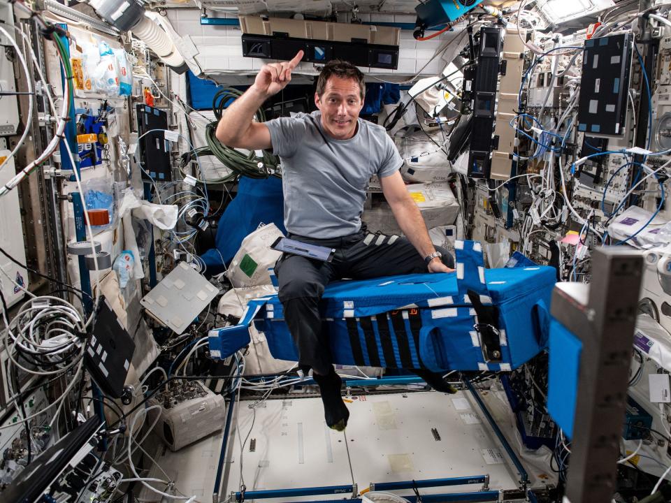 astronaut thomas pesquet poses for photo with one finger in the air while straddling floating equipment on the space station