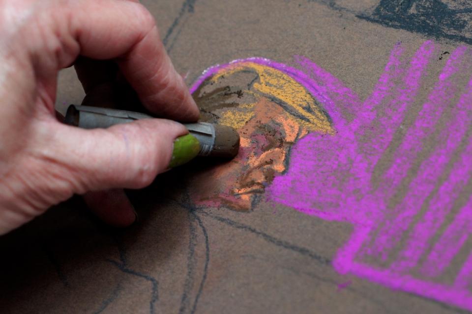 A hand sketching Donald Trump's face with chalk pastels.