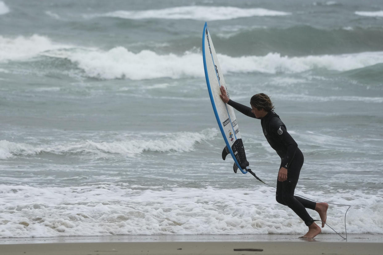 A surfer pushes his board in to the wind on Friday, Feb. 24, 2023, in Huntington Beach, Calif. California and other parts of the West faced heavy snow and rain Friday from the latest winter storm to pound the U.S. (AP Photo/Ashley Landis)