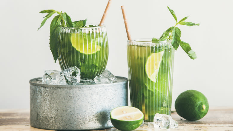 Two green cocktails garnished with herbs and limes