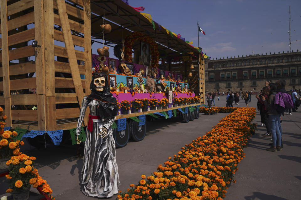 People pose for photos next to a Catrina sculpture next to a boxcar at the Zocalo square during celebrations ahead of the Day of the Dead in Mexico City, Tuesday, Oct. 31, 2023. (AP Photo/Marco Ugarte)