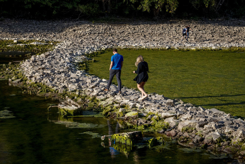 People walk over a stone dam, that is normally covered by water, towards the "Maeuseturm" (mice tower) in the middle of the river Rhine in Bingen, Germany, Friday, Aug. 12, 2022. The Rhine carries low water after a long drought period. (AP Photo/Michael Probst)