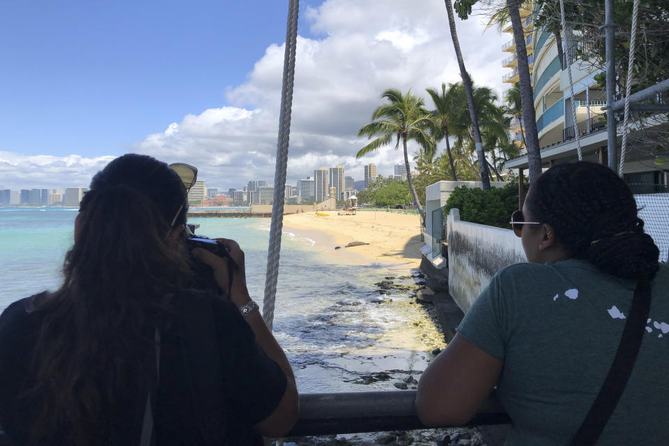 People look out toward Kaimana Beach at a Hawaiian monk seal and her pup that was born this past week in Honolulu, Thursday, April 20, 2023. Officials fenced off a large stretch of a popular Waikiki beach to protect the seal and her days-old pup. The unusual move highlights the challenges of protecting endangered species in a state that attracts millions of travelers every year. (AP Photo/Audrey McAvoy)