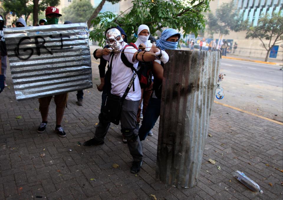 A masked demonstrator aims his slingshot loaded with a marble at Bolivarian National Guards during anti-government protests in Caracas, Venezuela, Sunday, March 2, 2014. Since mid-February, anti-government activists have been protesting high inflation, shortages of food stuffs and medicine, and violent crime in a nation with the world's largest proven oil reserves. (AP Photo/Rodrigo Abd)