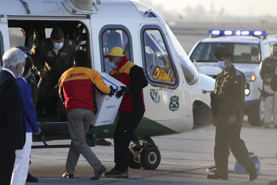 Los trabajadores llevan una caja que contiene las vacunas Pfizer COVID-19 a un helicóptero para su distribución en todo el país en el Aeropuerto Internacional Merino Benítez en Santiago, Chile, el jueves 24 de diciembre de 2020. El primer envío de la vacuna Pfizer contra COVID-19 llegó a Chile el jueves temprano desde Bélgica. (AP Foto/Esteban Felix)