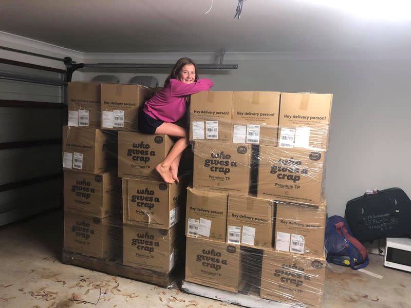 A girl sits on top of boxes containing toilet paper in Toowoomba