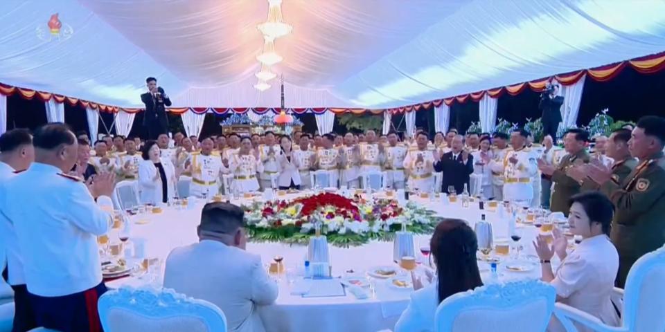 A general view from behind Kim Jong Un's chair at a banquet in Pyongyang, showing many people standing and applauding, on August 27, 2023.