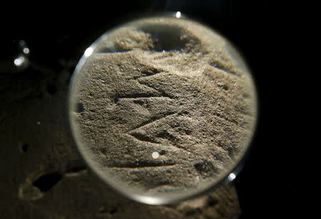 An inscription on an Etruscan stele is seen through a magnifying glass in a restoration centre in Florence, Italy, April 20, 2016. REUTERS/Remo Casilli