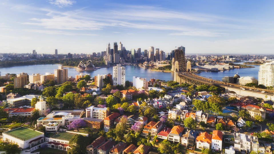 Sydney Harbour lower north Shore against city CBD waterfront around Circular quay and the Sydney Harbour bridge over red roofs of low-rise residential houses in aerial view.