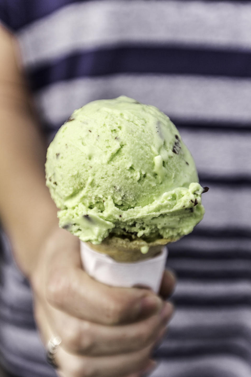 A kid holding a cone of mint ice cream.