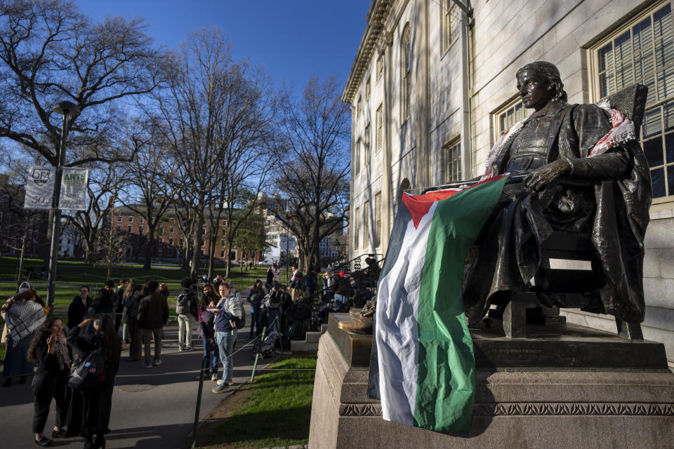 Students protesting against the war in Gaza, and passersby walking through Harvard Yard, are seen next to the statue of John Harvard, the first major benefactor of Harvard College, draped in the Palestinian flag, at an encampment at Harvard University in Cambridge, Mass., on Thursday, April 25, 2024. (AP Photo/Ben Curtis)