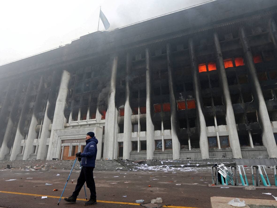 A man stands in front of the mayor's office building in Almaty, Kazakhstan, which was torched this week during protests triggered by fuel price increases.  (Pavel Mikheyev/Reuters - image credit)