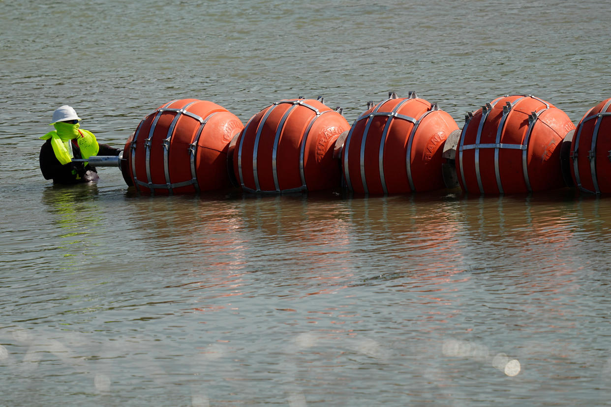 A worker helps deploy a string of large buoys to be used as a border barrier at the center of the Rio Grande near Eagle Pass, Texas, on July 11, 2023.  (Eric Gay / AP)