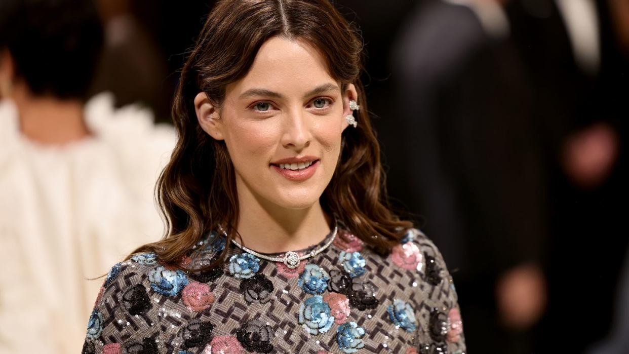 riley keough smiling in front of a crowd of people in the background