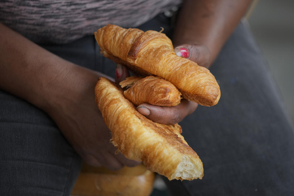 A woman holds croissants handed to children waiting for an eyesight examination performed by volunteer ophthalmologists, in Nucsoara, Romania, Saturday, May 29, 2021. Dozens of disadvantaged young Romanian children got a chance to get their eyesight examined for the first time in their lives during an event arranged by humanitarian organization Casa Buna, or Good House, which has played a prominent role in supporting the local children's lives throughout the pandemic. (AP Photo/Vadim Ghirda)