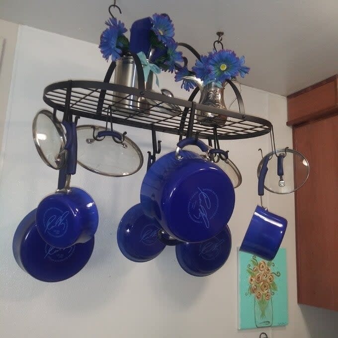 A hanging pot rack with blue pots, pans, and floral decor in a kitchen setting