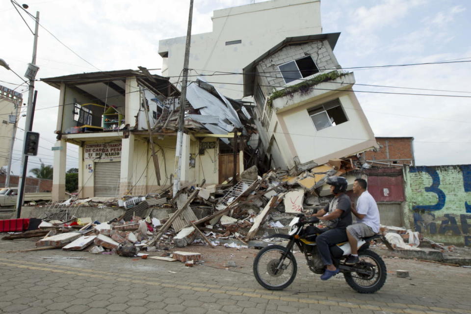 Men ride by damaged buildings