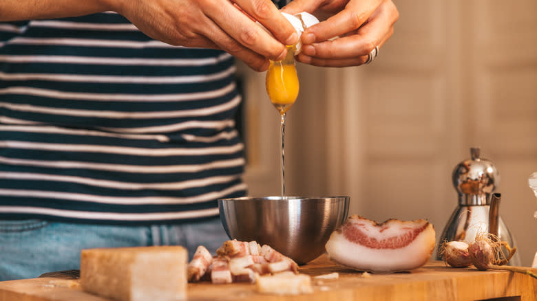 cook separating eggs alongside carbonara ingredients