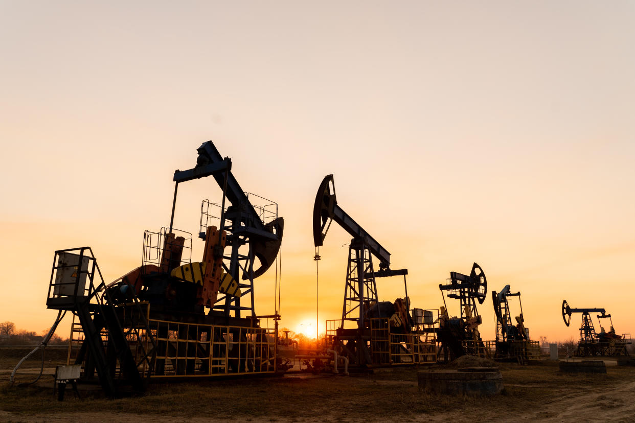 The silhouette of oil pumps on a beautiful sunset sky with sun setting in between them.Siberia. Oil and gas production