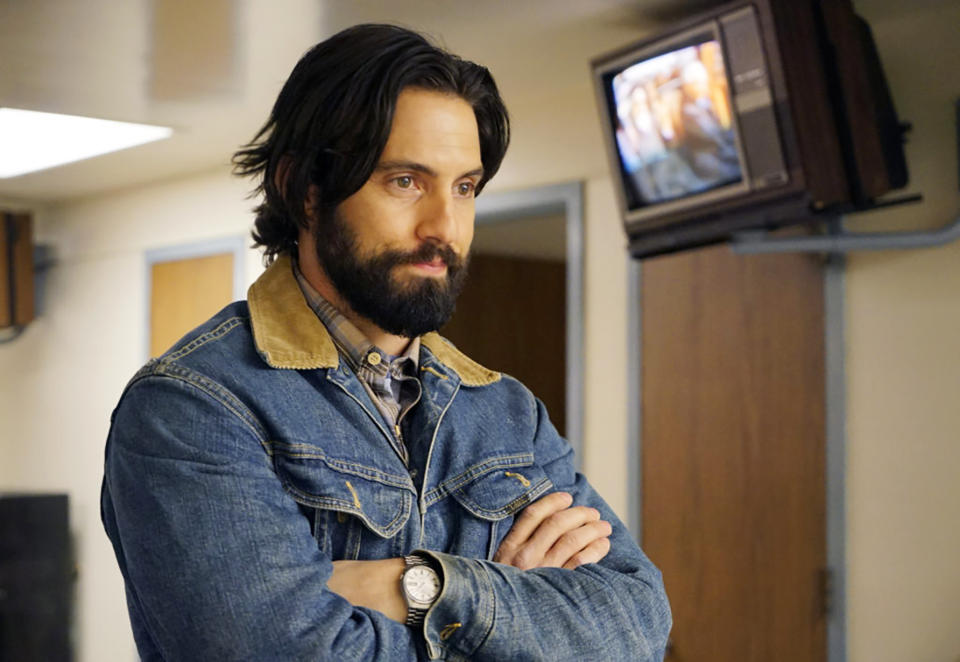 Milo Ventimiglia stands with arms crossed, wearing a denim jacket with a beige collar, in what appears to be a waiting room