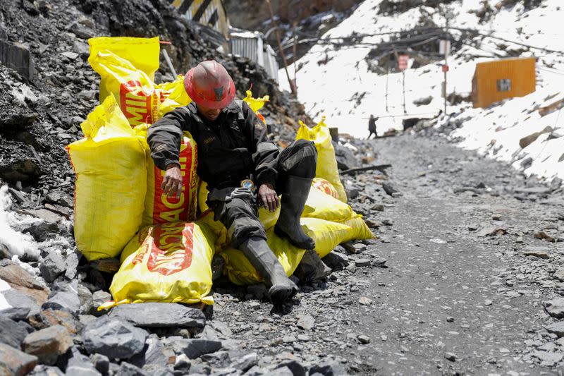 An artisanal gold miner sits on sacks of stones from a gold mine, before it is processed to extract gold, in La Rinconada, in the Andes