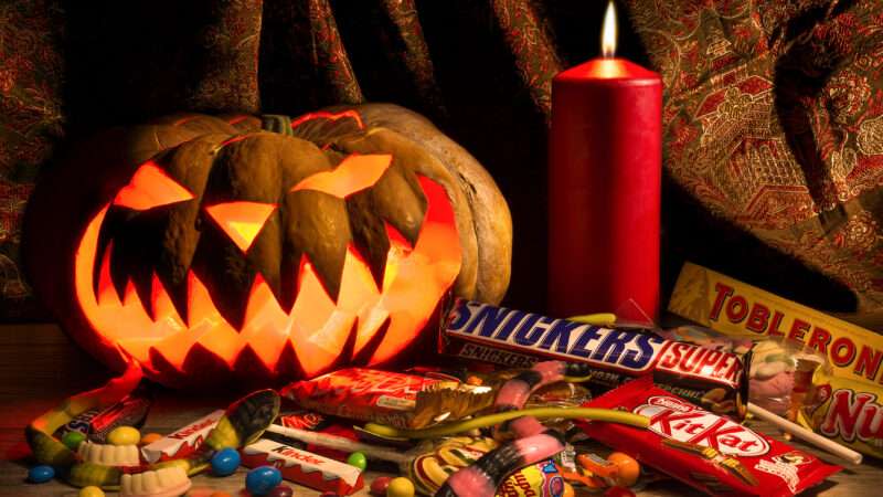 A lit Jack-o-lantern sits next to a candle and some Halloween candy
