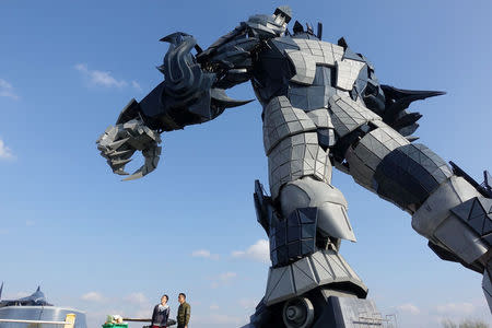 Staff members stand underneath a giant robot statue at the Oriental Science Fiction Valley theme park in Guiyang, Guizhou province, China November 16, 2017. REUTERS/Joseph Campbell/Files