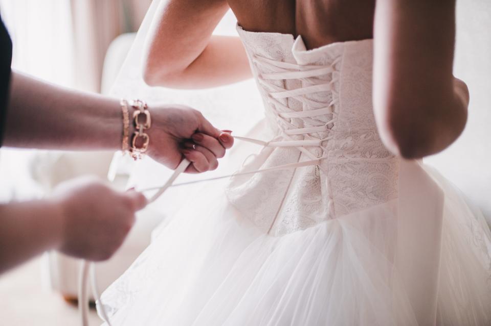 Bridesmaid helping the bride to wear a dress