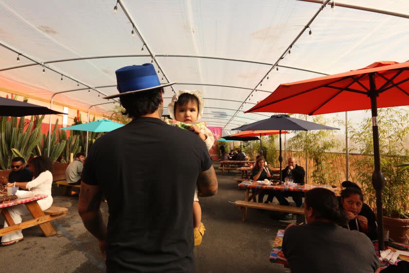 LOS ANGELES, CA - NOVEMBER 25, 2020 - Gilberto Marquez and his 11 month-old daughter Cynthya, walk to their table at Guelaguetza restaurant in Los Angeles on November 25, 2020. The area was part of their parking lot that the restaurant had converted to accommodate outdoor dining. Wednesday was the last day the restaurant would be allowed outdoor dining. With coronavirus cases continuing to soar across the state, a divided L.A. County officials have imposed a ban for at least three weeks all in-person dining and restrict restaurants - along with breweries, wineries and bars - just to takeout and delivery service beginning at 10 p.m. Wednesday. The announcement came after the county's five-day average of new coronavirus cases topped 4,000, a threshold officials had set for implementing the restriction. (Genaro Molina / Los Angeles Times)