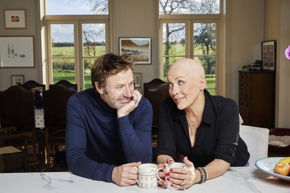 Pictured: Sarah Beeny and Graham Swift in their kitchen sitting on stools drinking tea/coffee - Sarah Beeny Vs Cancer (Channel 4)