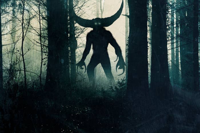 A shadowy, horned creature stands ominously in a misty forest, with large glowing eyes, amidst towering trees. No visible humans or text in the scene