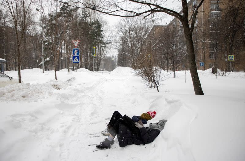 Young women lie on the ground in a street during snowfall in Moscow