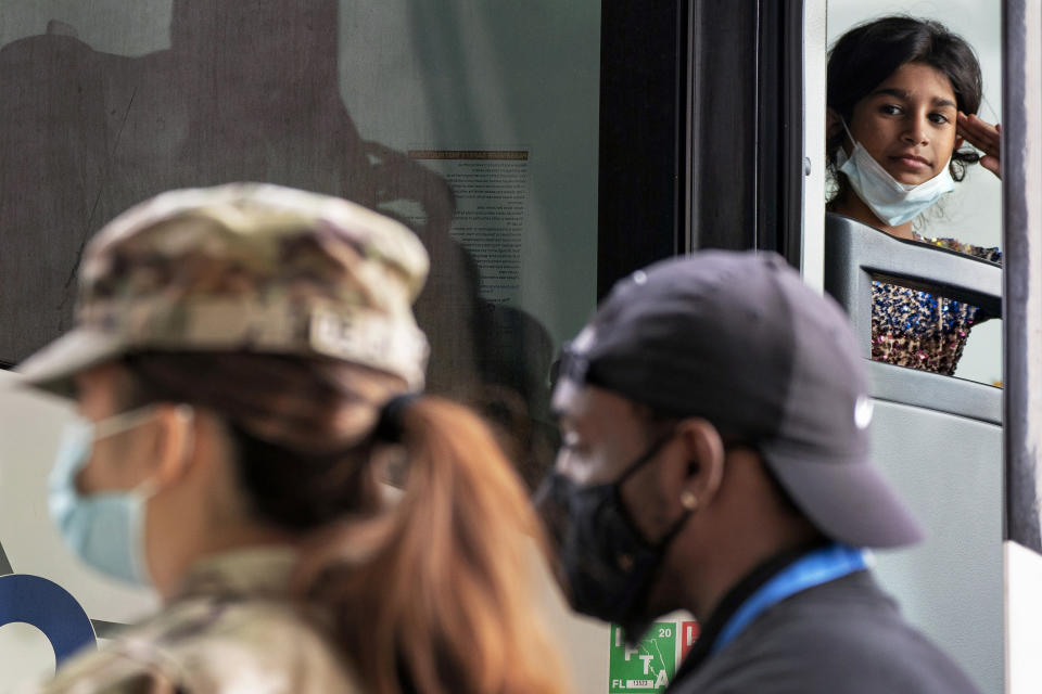 A girl leans against her fingertips while looking out at a female U.S. soldier, as families evacuated from Kabul, Afghanistan, board a bus after they arrived at Washington Dulles International Airport, in Chantilly, Va., on Tuesday, Aug. 31, 2021. (AP Photo/Jacquelyn Martin)