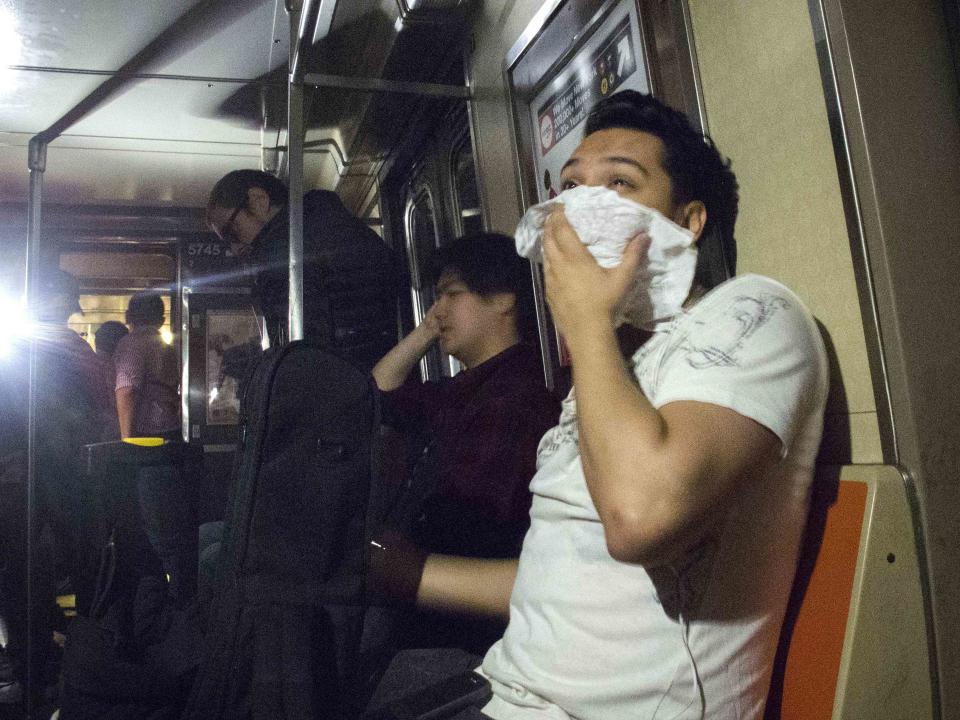 A passenger, lit by mobile phones, covers his nose and mouth to avoid smoke inhalation after the "F" train derailed in the Woodside neighborhood located in the Queens borough of New York May 2, 2014. (REUTERS/Connie Wang)