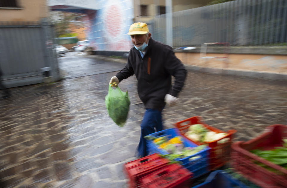 Domenico Zoccoli, 80, walks by a fruit and vegetable stand in an open air market where he works, in Rome, Wednesday, Dec. 2, 2020. In Italy, which has the world's second-oldest population, many people in their 70s and older have kept working through the COVID-19 pandemic. From neighborhood newsstand dealers to farmers bring crops to market, they are defying stereotypic labels that depict the old as a monolithic category that's fragile and in need of protection. (AP Photo/Alessandra Tarantino)