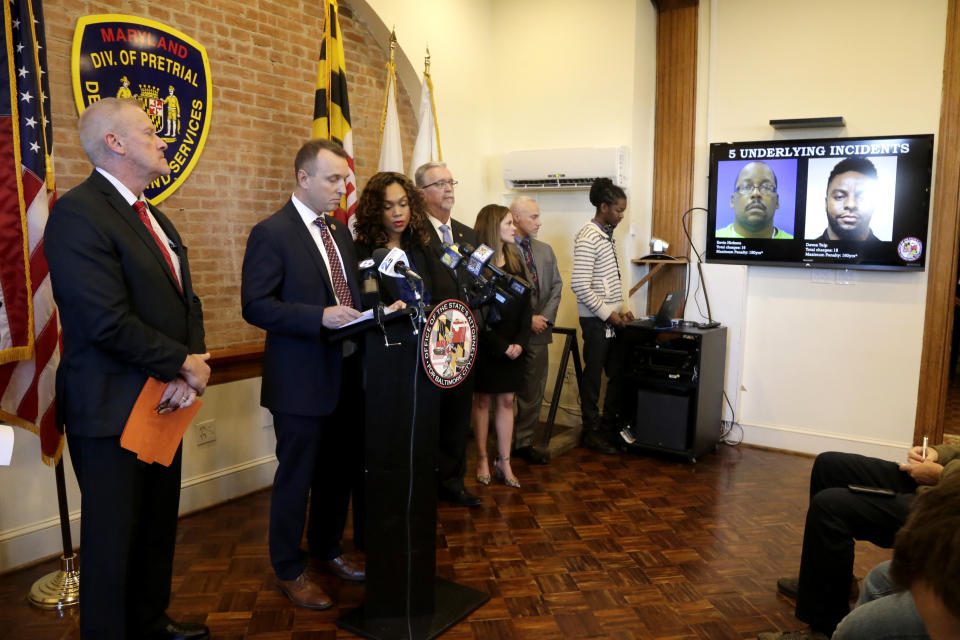 Maryland Assistant State Attorney Patrick Seidel, second from left, stands next to State Attorney Marilyn Mosby, third from right, as a monitor displays two of the correction officers indicted during a news conference, Tuesday, Dec. 3, 2019, in Baltimore. Twenty five correction officers, most of whom were taken into custody earlier in the day, are charged with using excessive force on detainees at state-operated Baltimore pretrial correctional facilities. (AP Photo/Julio Cortez)