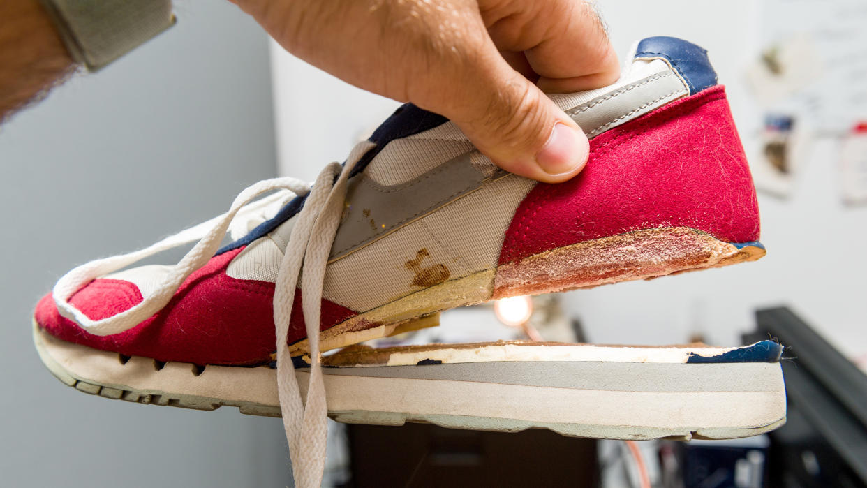  Man holding sports shoe with sole falling off. 