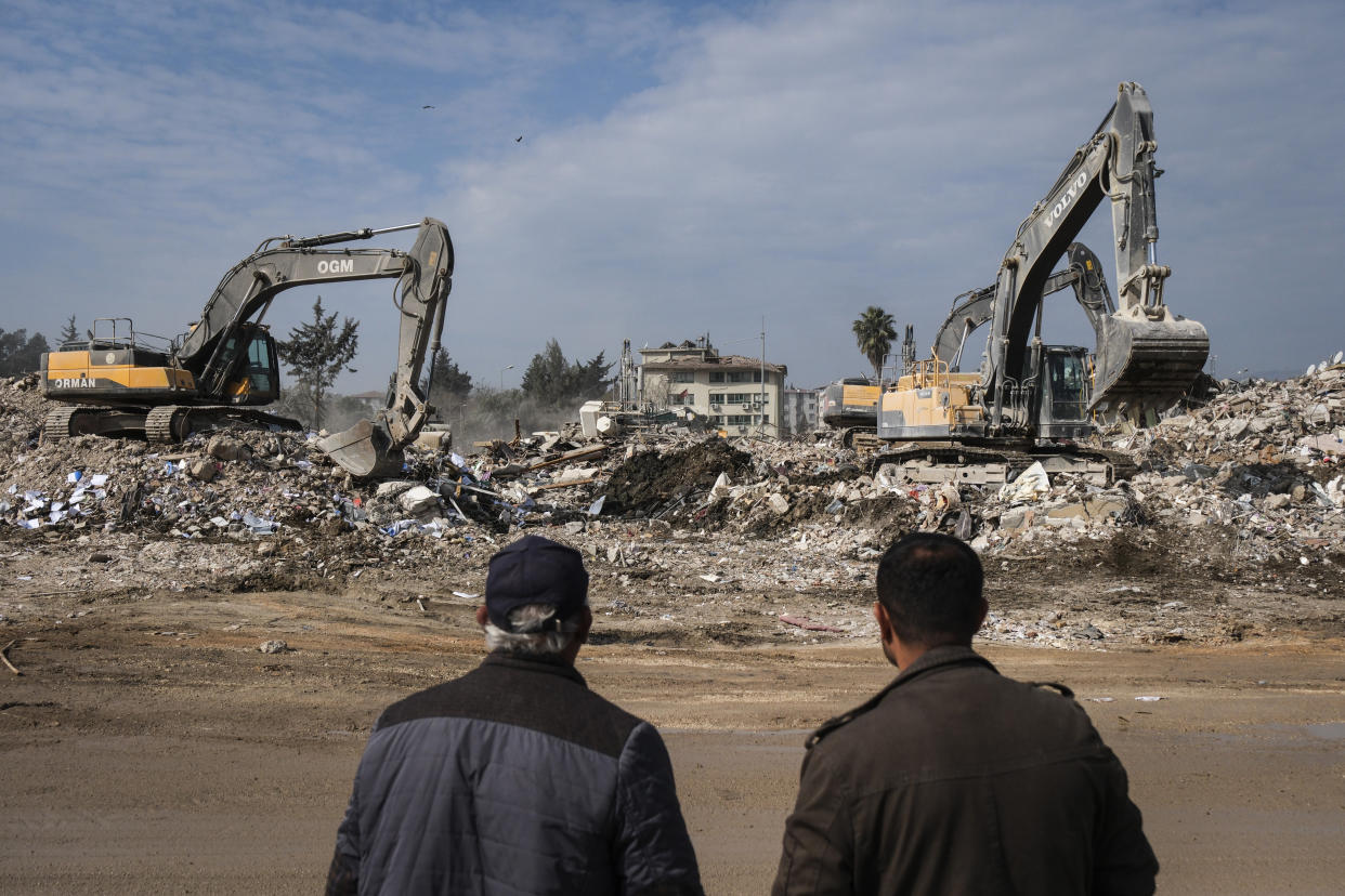 Two men watch the rubble removal process in Hatay, Turkey.