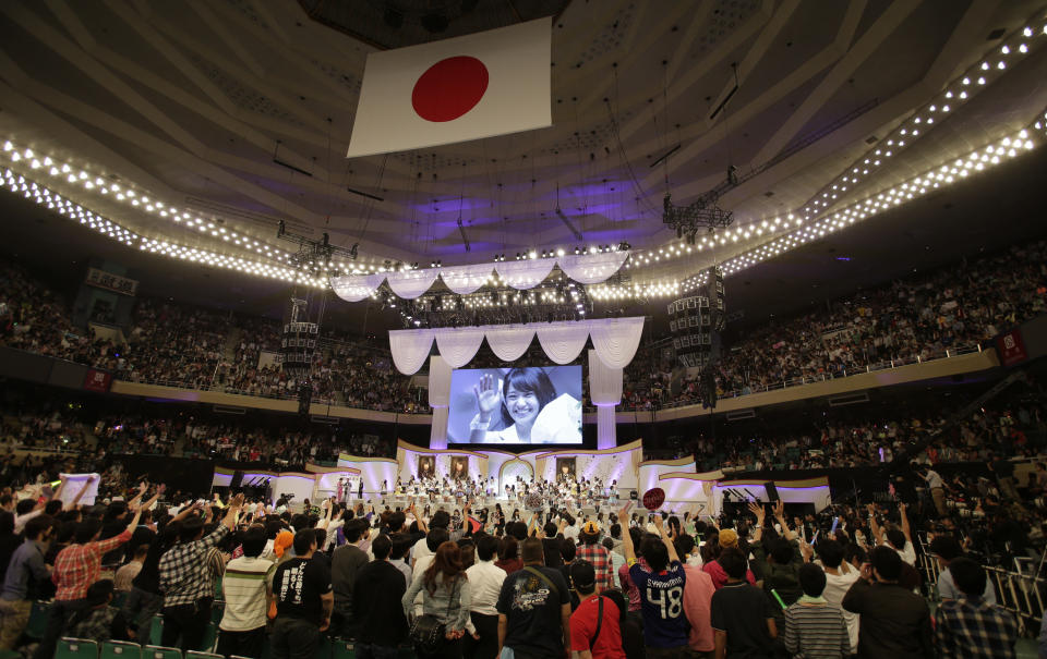 FILE - In this June 6, 2012 file photo, an image of Japan’s all-girl pop idol group AKB48 member Yuko Oshima waving at fans is shown on the screen after she won the annual AKB48 popularity poll in Tokyo. More than 60 girls and young women, split into four teams, make up what is arguably Japan's most popular pop group. It performs almost every day, has spawned affiliate groups across the country and has recently given rise to sister mega-groups in China and Indonesia. (AP Photo/Shizuo Kambayashi, File)