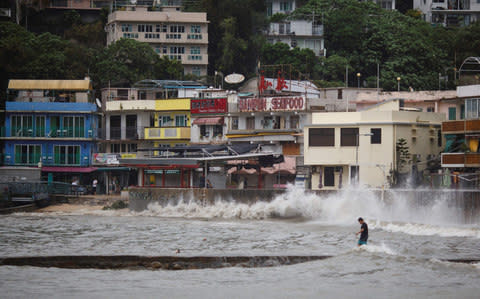 A man walks out on a low-lying wharf while large waves caused by Typhoon Hato break along the waterfront in Hong Kong's Lamma Island - Credit: AFP