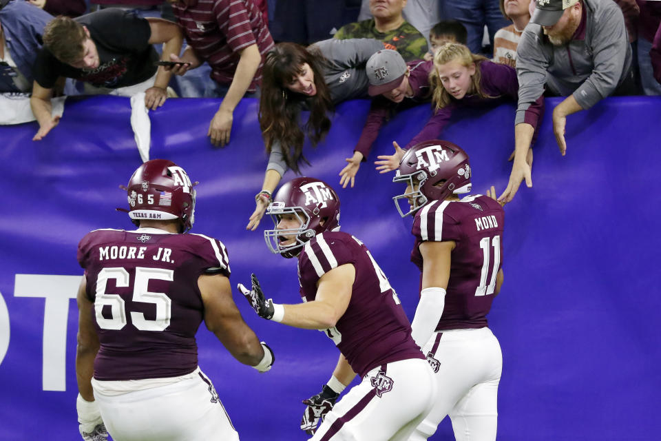 Texas A&M offensive lineman Dan Moore Jr. (65) and tight end Ryan Renick, middle, celebrate as quarterback Kellen Mond (11) high-five fans in the stands after Mond's touchdown during the second half of the Texas Bowl NCAA college football game against Oklahoma State on Friday, Dec. 27, 2019, in Houston. (AP Photo/Michael Wyke)