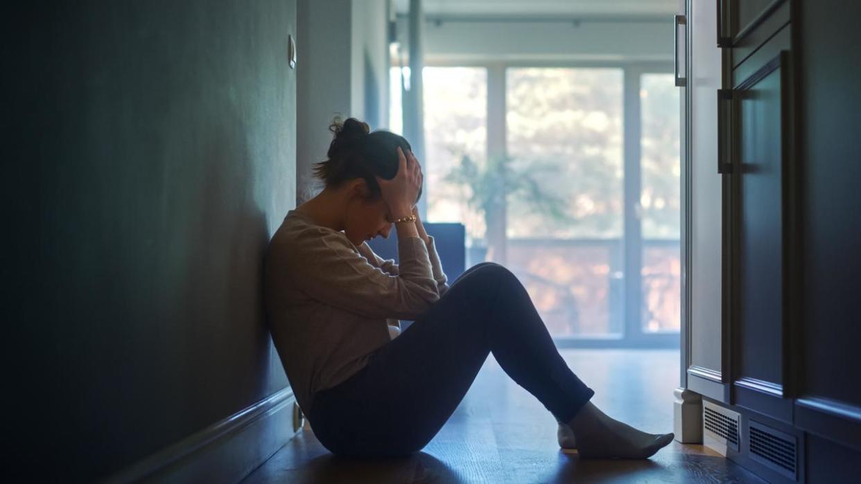 Sad Young Woman Sitting on the Floor In the Hallway of Her Appartment, Covering Face with Hands. Atmosphere of Depression, Trouble in Relationship, Death in the Family. Dramatic Bad News Moment