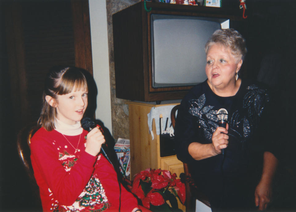 Girl and older woman singing into microphones, casual home setting with a TV in the background