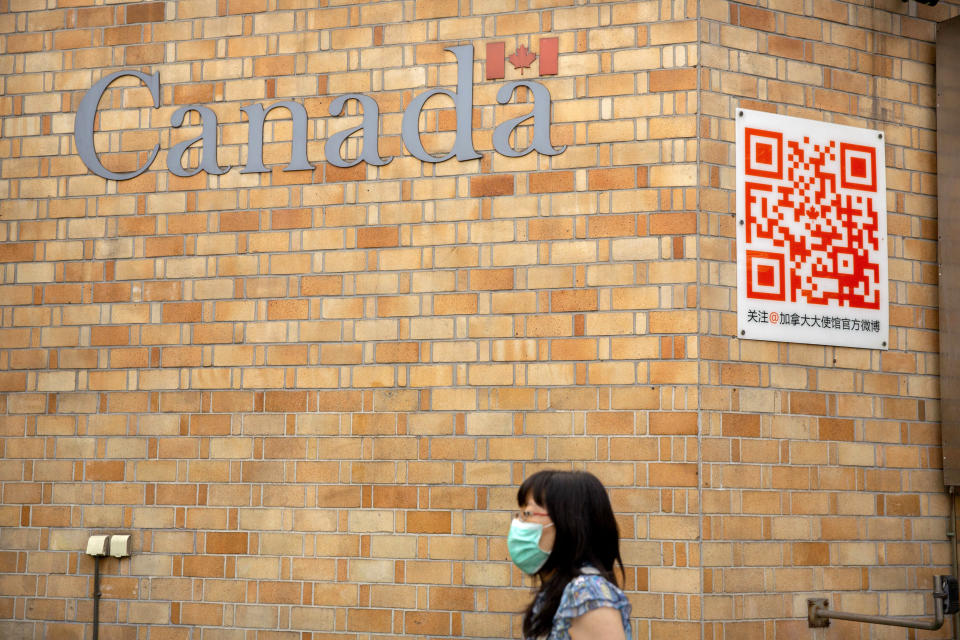 A woman wearing a face mask to help protect against the coronavirus walks past the Canadian Embassy in Beijing, Thursday, Aug. 6, 2020. China has sentenced a Canadian citizen to death on charges of manufacturing the drug ketamine amid heightened tension between the two countries. (AP Photo/Mark Schiefelbein)