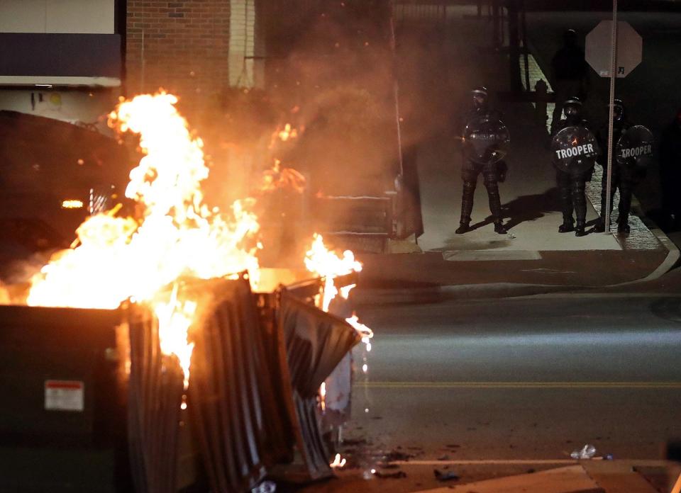 Officers in riot gear watch as a pair of dumpsters burn on South Main Street in Akron during protests Sunday.