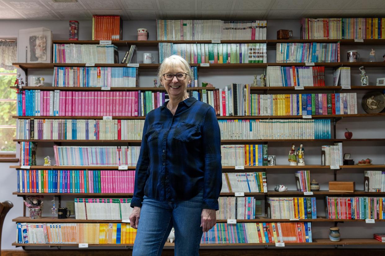 Bestselling author Leigh Michaels stands in front of bookshelves containing original copies of her romance novels, which include translated versions and anime. More than 35 million copies of her books have been printed, in 27 languages and more than 120 countries.